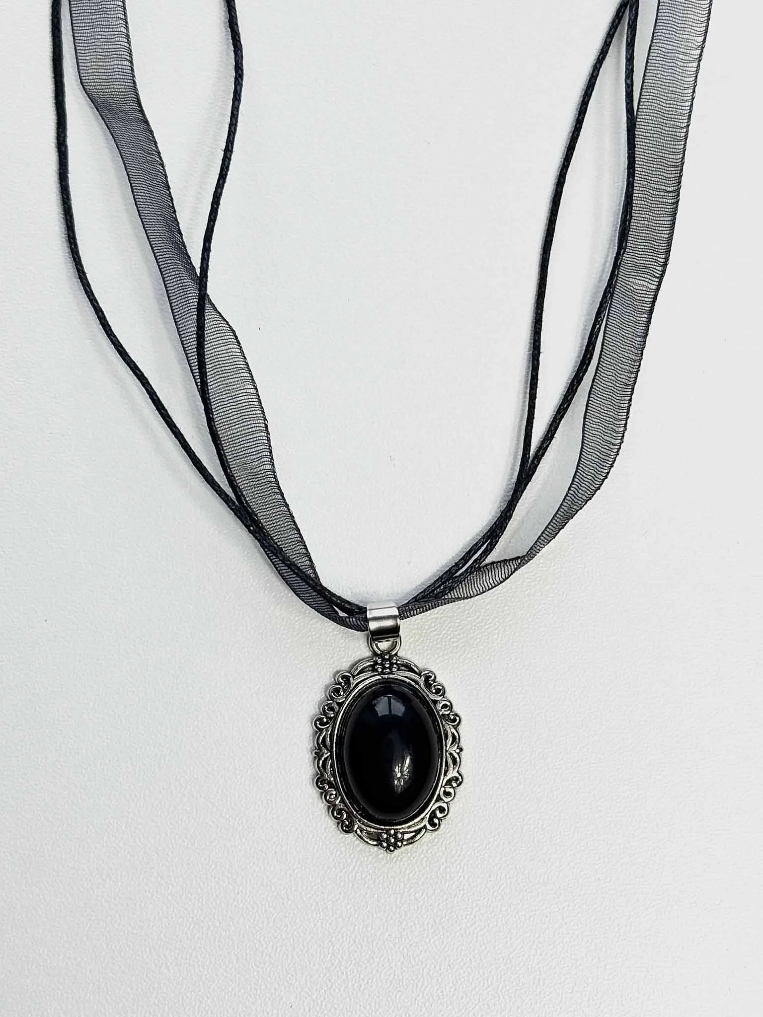 Melnā obsidiāna kulons "Ēnu vēstnesis" uz gaišas virsmas no Ginella
